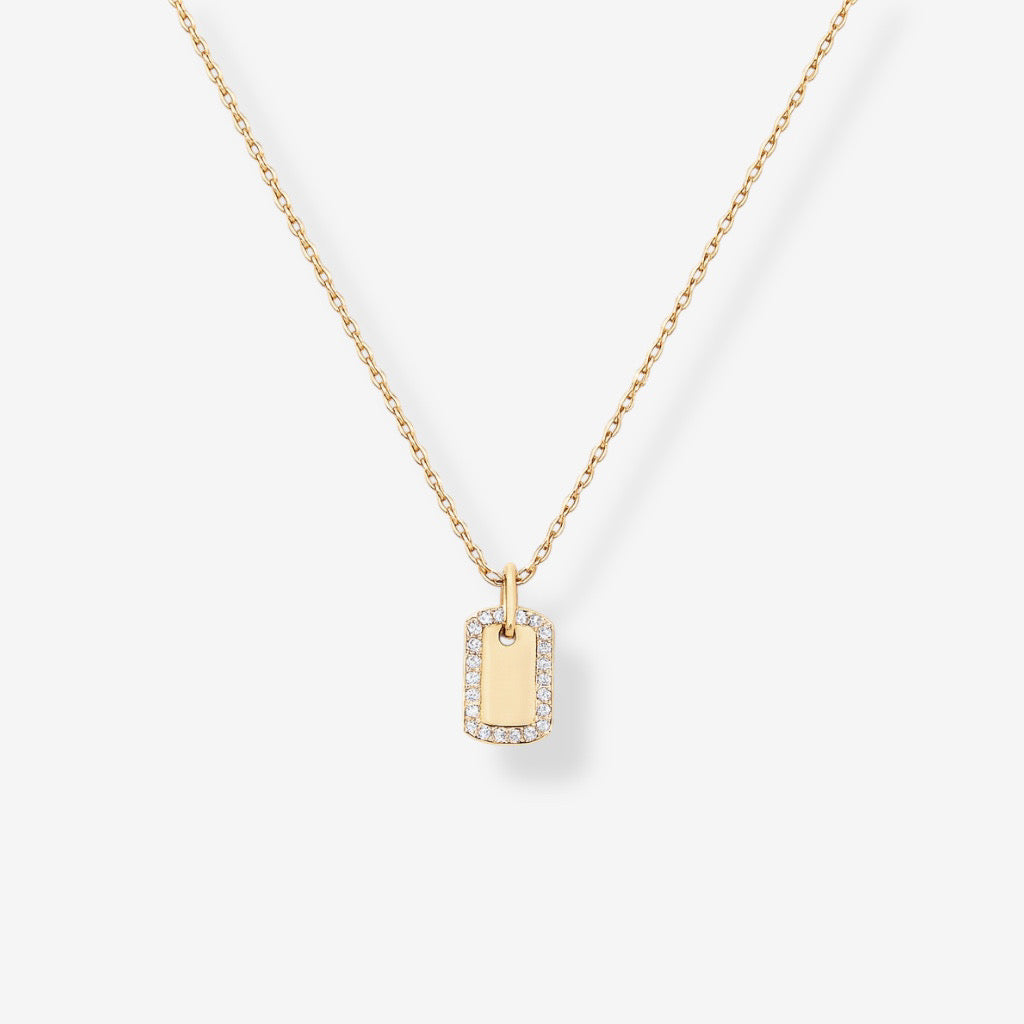 The Dainty Dog Tag Necklace – Gold features a small rectangular pendant edged with sparkling gems, suspended from a fine gold chain, shown against a white background.