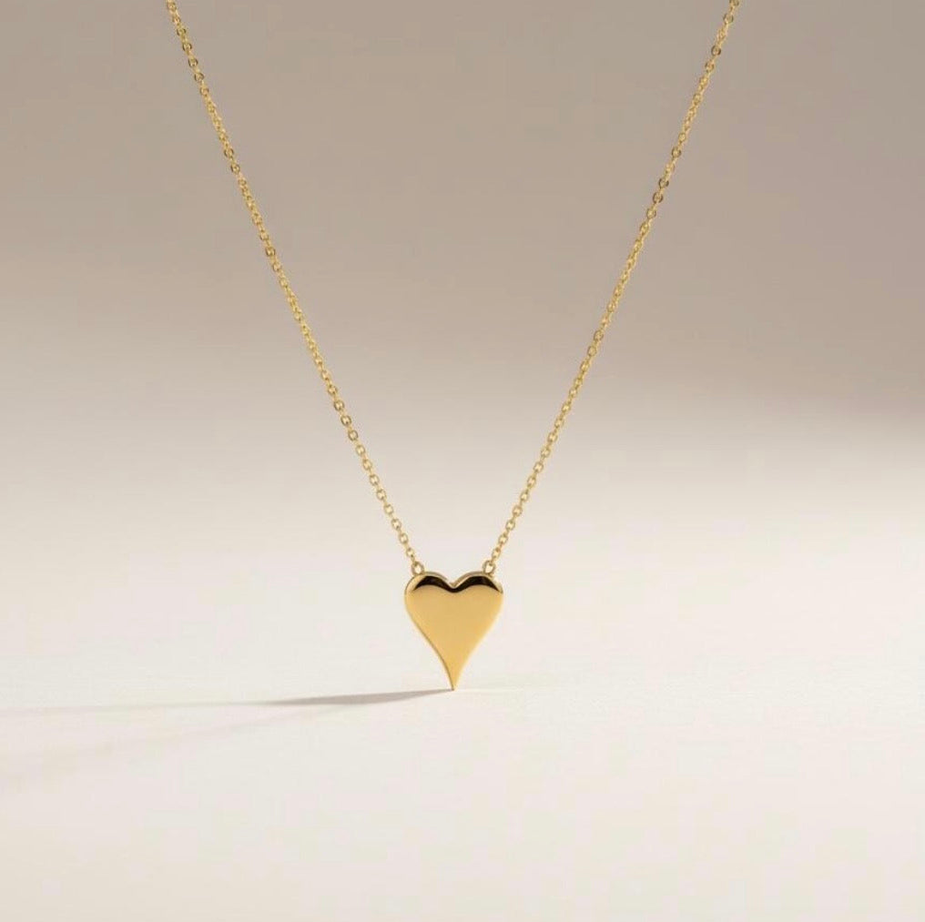 Terry gold heart pendant necklace styled on neutral background with delicate gold chain