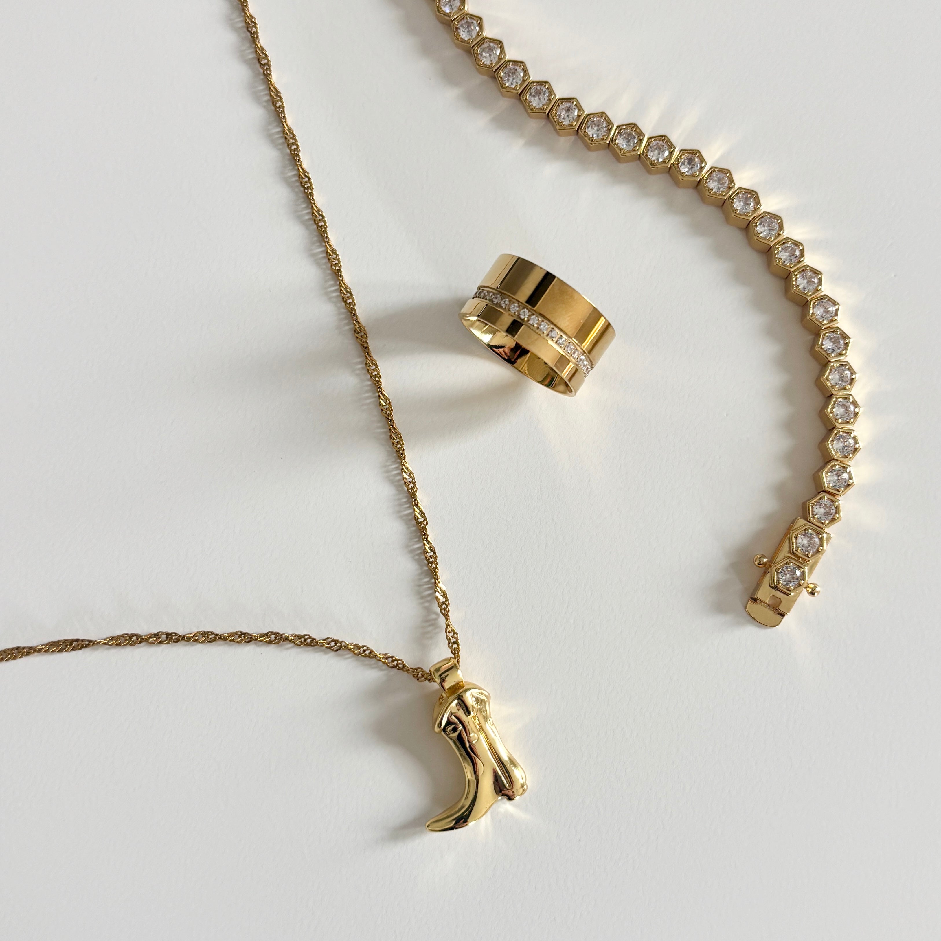 Boots & Broadway Pendant Necklace in gold shown in flat lay on neutral surface featuring cowgirl boot charm paired with other Luxxy pieces