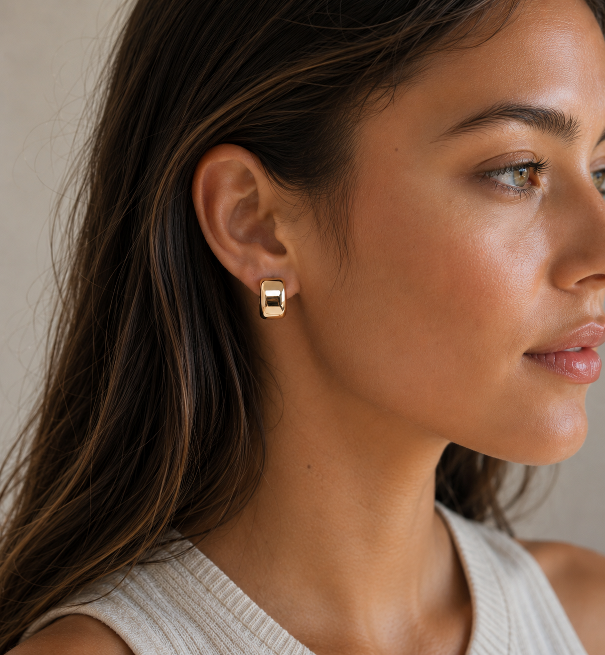 Young woman with long dark hair wearing Brookes Curved Stud Earrings in gold minimalist polished gold earrings against light background