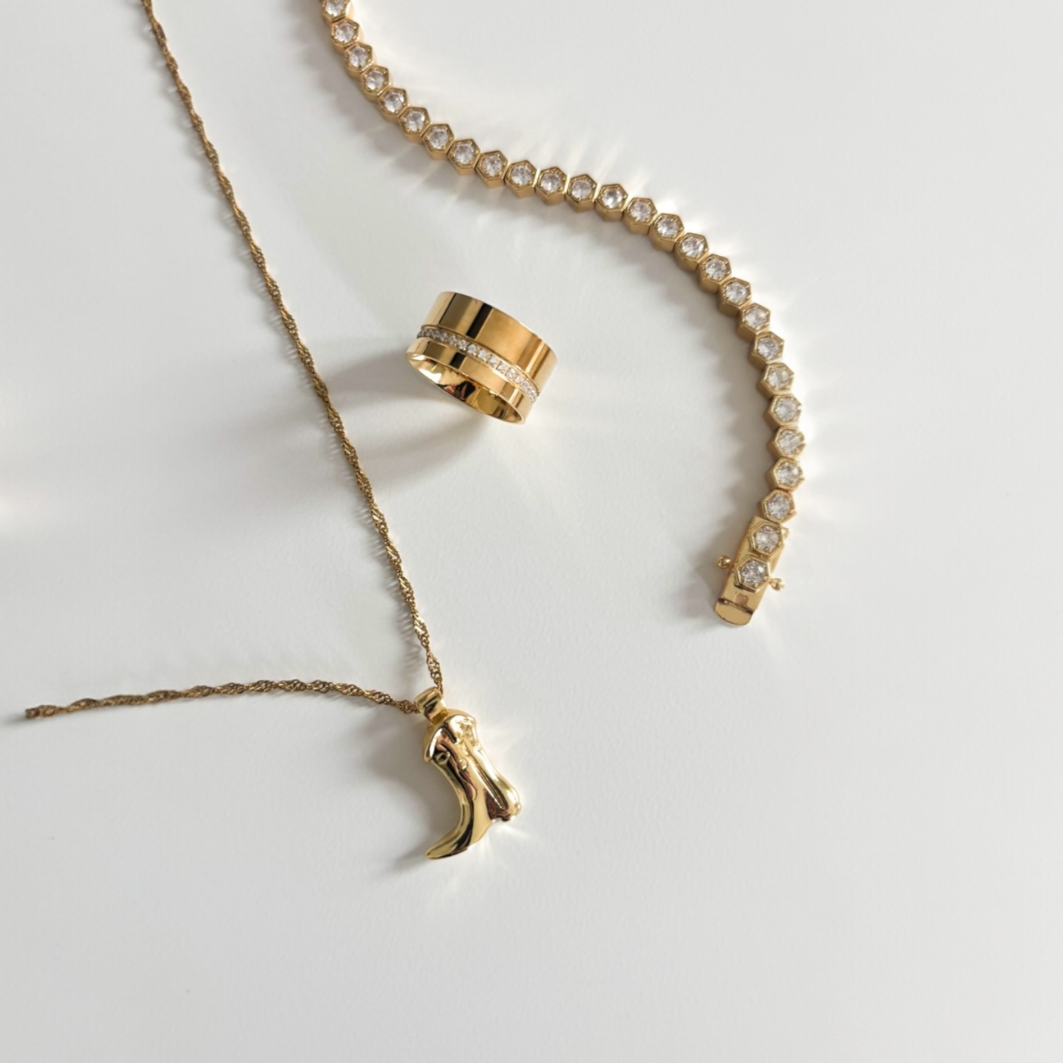 Flat lay of the Celine cigar ring in gold styled with a tennis bracelet and pendant necklace on a neutral surface