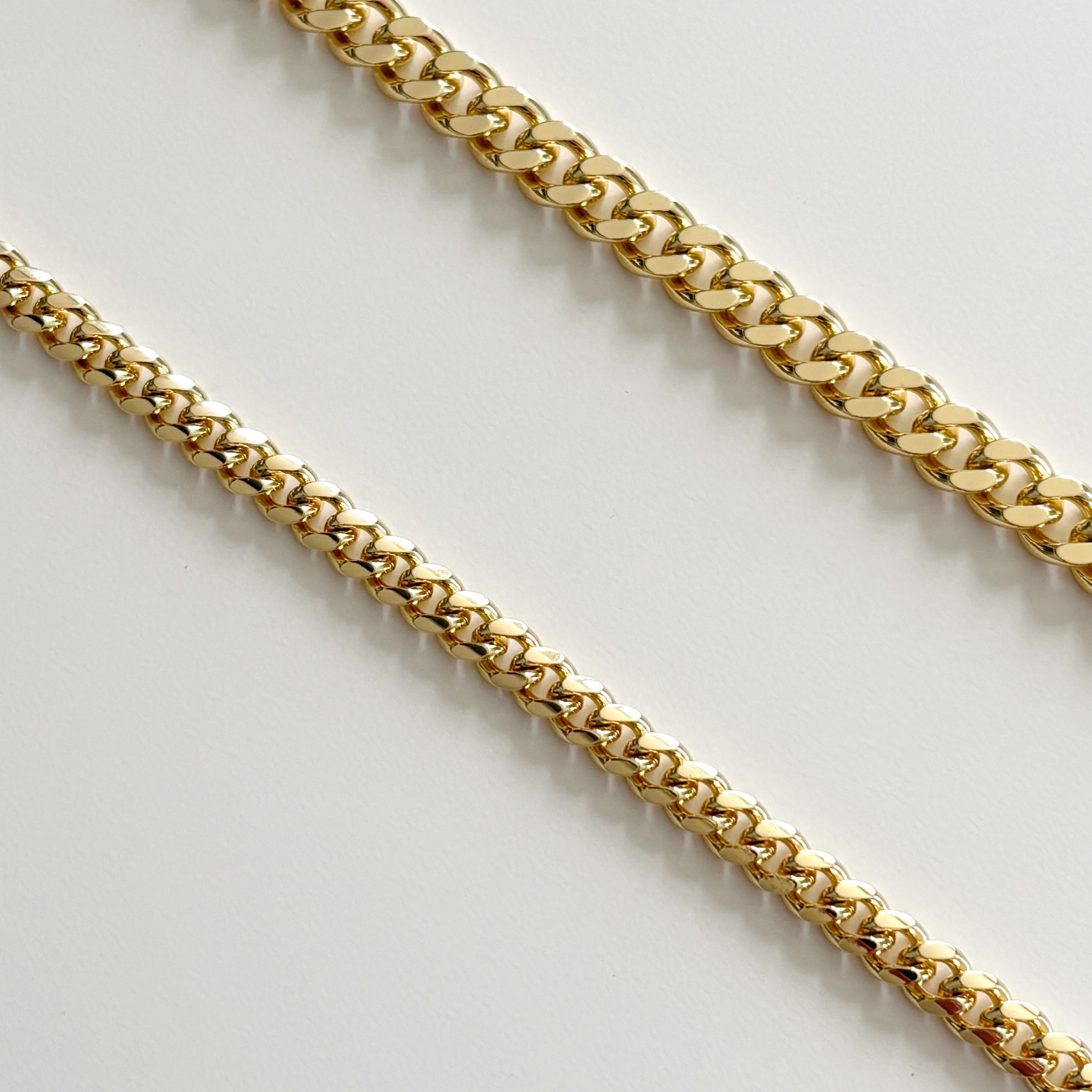 Luxxy close-up of gold curb chains on a light gray background | Affordable luxury jewelry by Luxxy