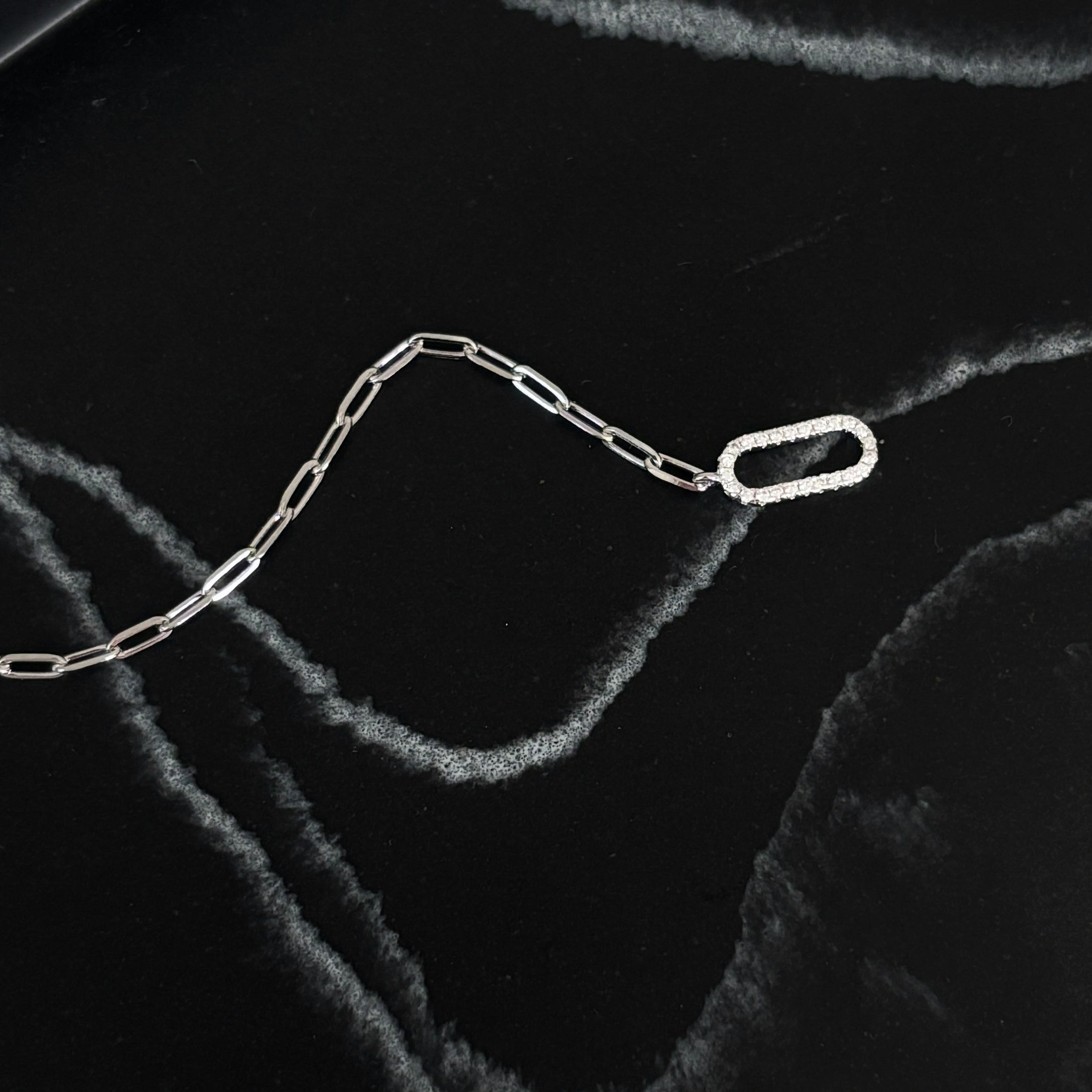 Luxxy dainty paperclip bracelet with oval micro pave toggle clasp in silver on textured background