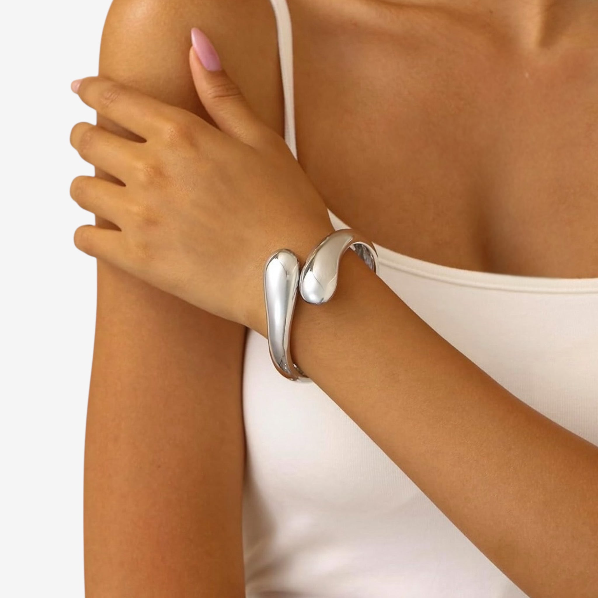 A woman in a white tank top shows off her left arm, styled with the Jade Snake Bangle. Her light pink manicured nails highlight the modern, sculptural silver bracelet, making it stand out elegantly.