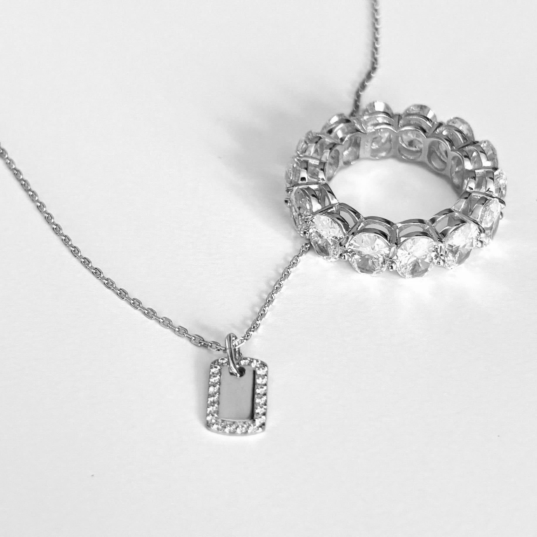 Luxxy silver micro pave dog tag necklace with sterling silver eternity ring on light grey background