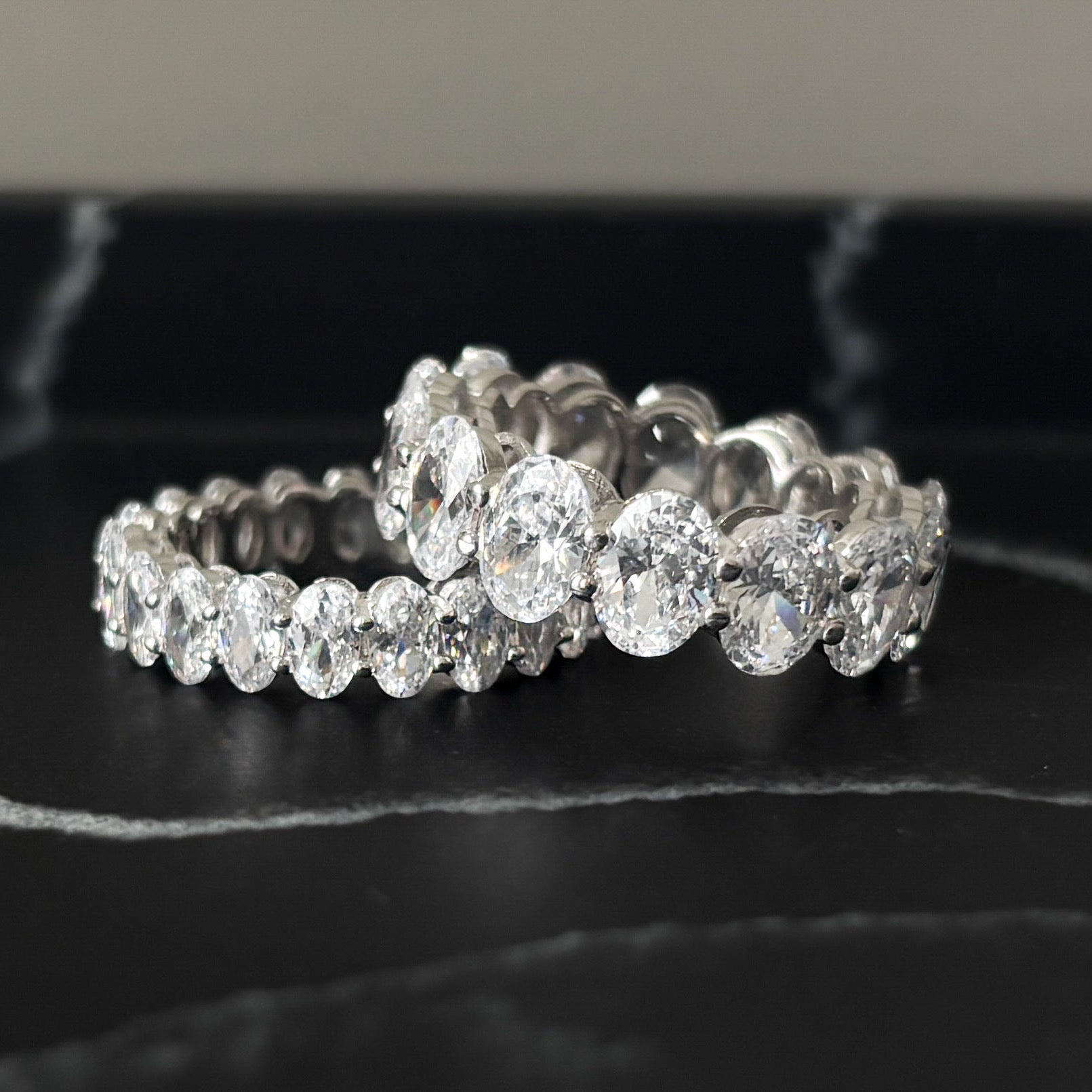 Close-up of Aria and Bella eternity rings in sterling silver on black marble background