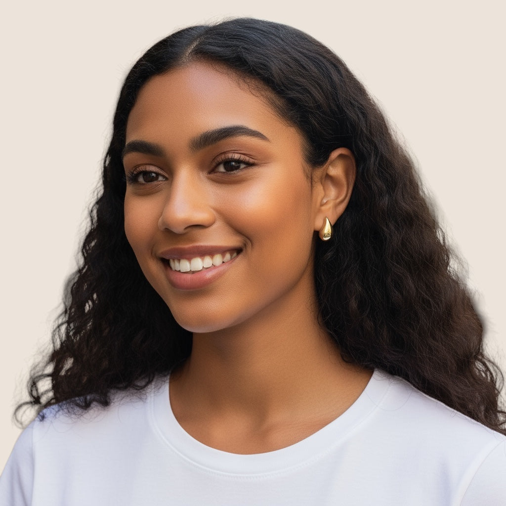 A young woman with long curly hair smiles warmly at the camera, wearing a white top and Demi Teardrop Earrings against a plain light background.