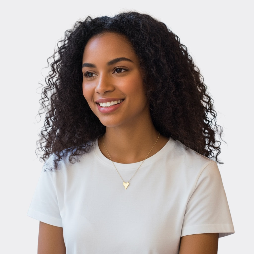 A young woman with curly hair smiles, wearing a white t-shirt and the Terry Heart Pendant Necklace, set against a plain light background.