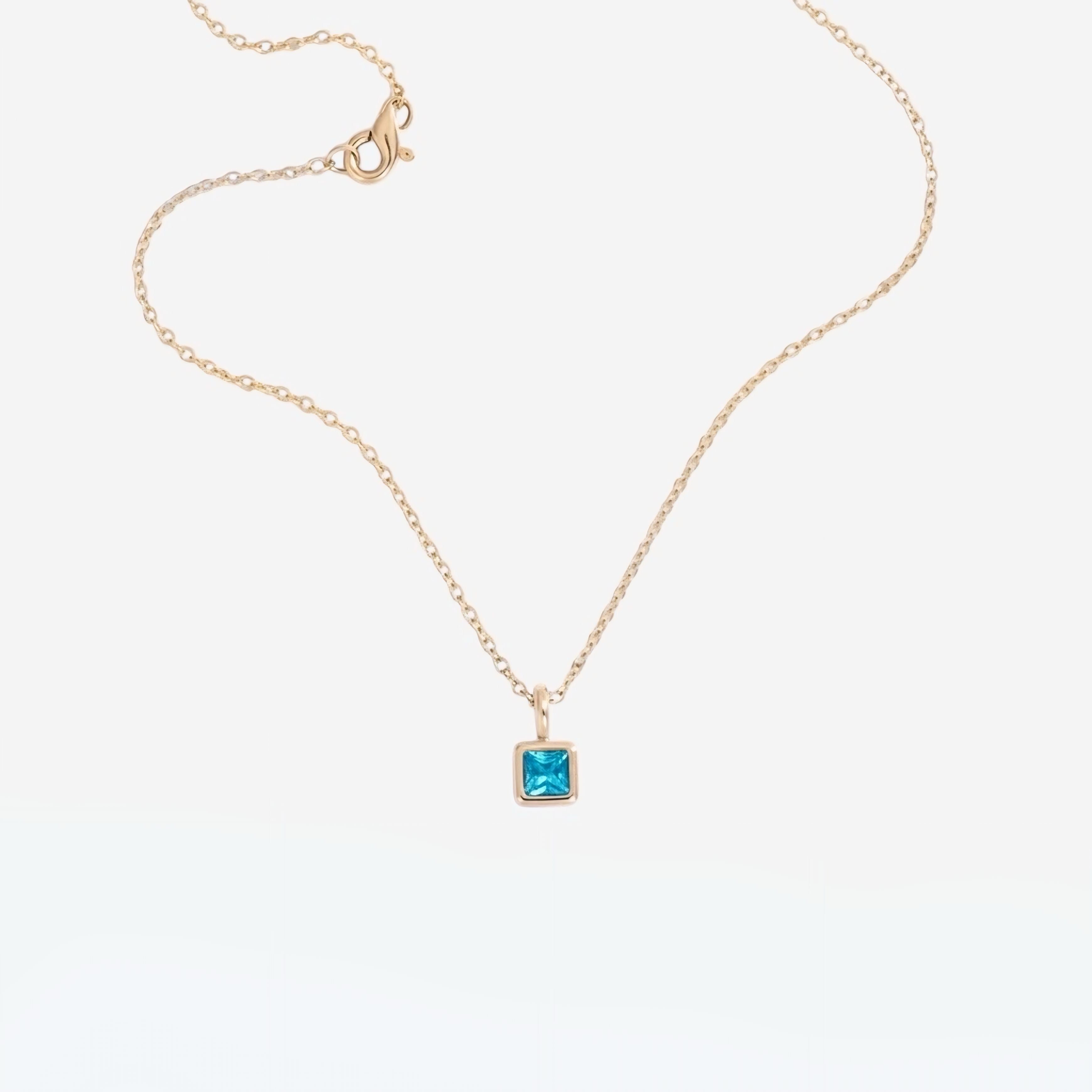 The Abel Birthstone Necklace features a delicate gold plated chain with a square blue birthstone pendant, shown against a plain white background.