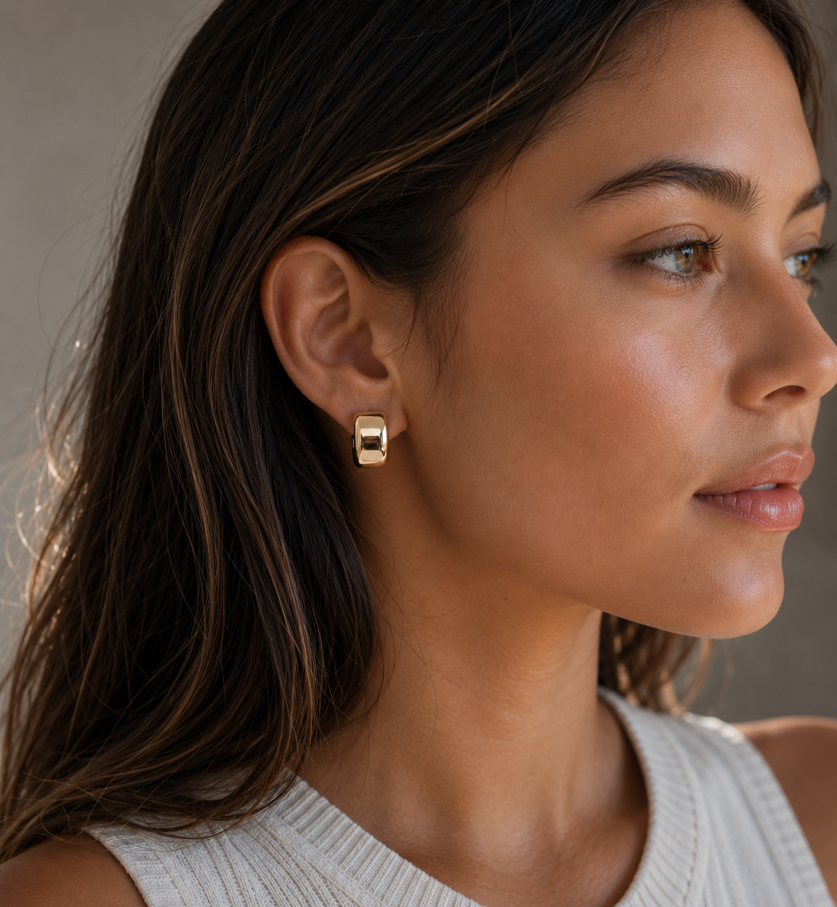 Close up of model wearing Brookes Gold Sculptural stud earrings against a neutral background 