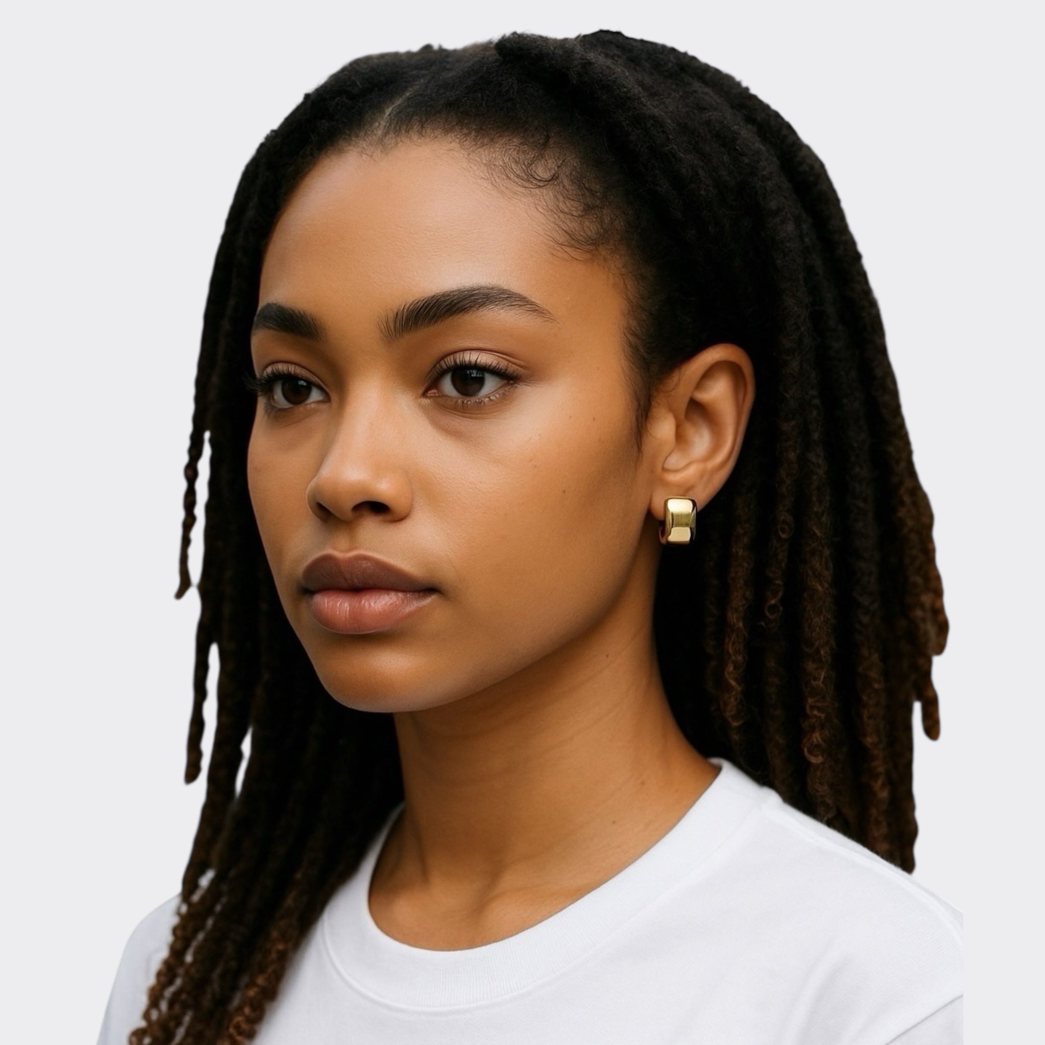 A young woman with long, dark dreadlocks wears a white shirt and Brookes Curved Stud Earrings in 14k gold plate, gazing calmly to the side against a plain light background.