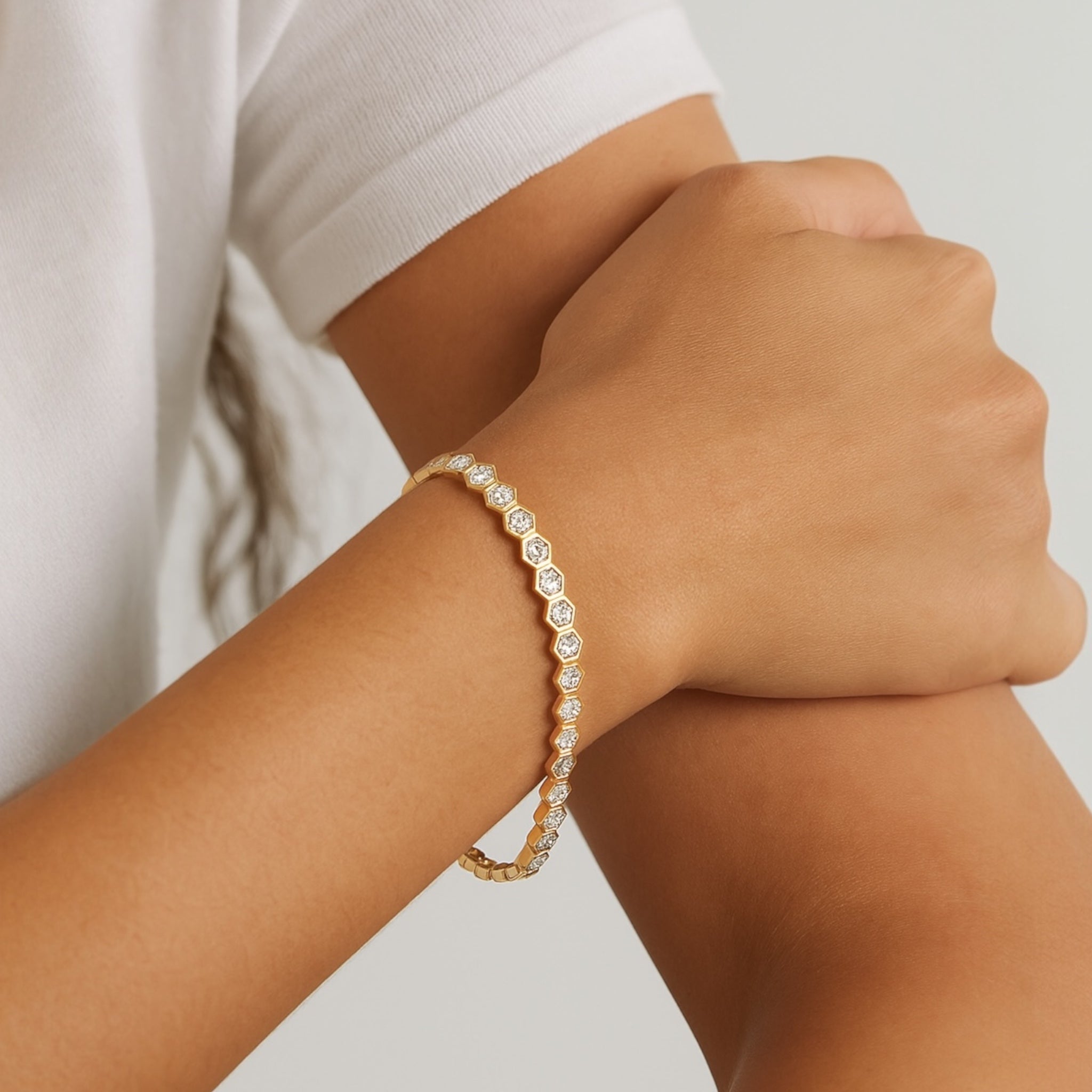 A person in a white short-sleeve shirt rests one arm on the other, showcasing the Hexagon Tennis Bracelet adorned with round, diamond-like stones.