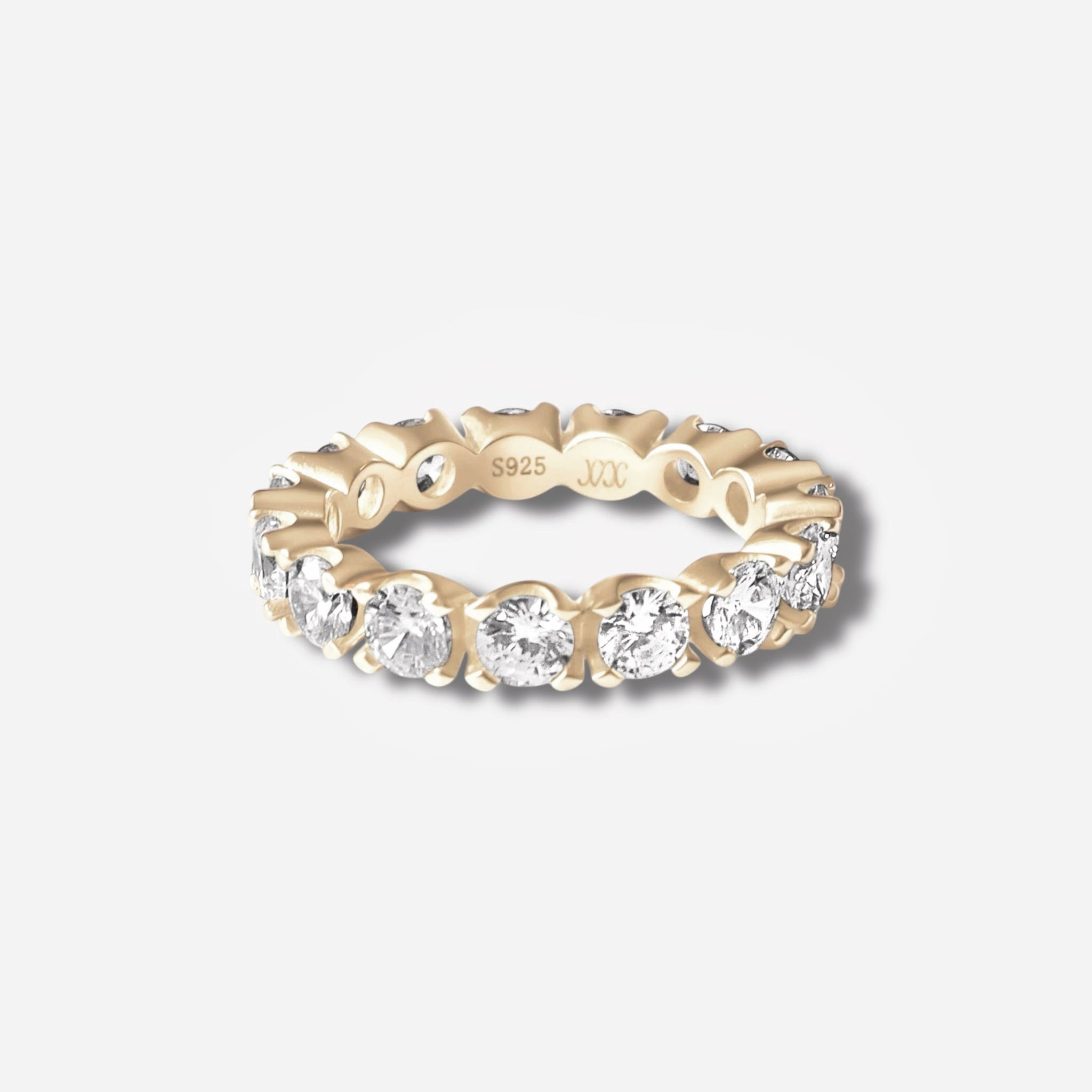 The Sydney Ring is a gold plated eternity band set with sparkling round simulated diamonds all around, featuring an inner band engraved with S925 and small markings. Displayed on a plain white background.