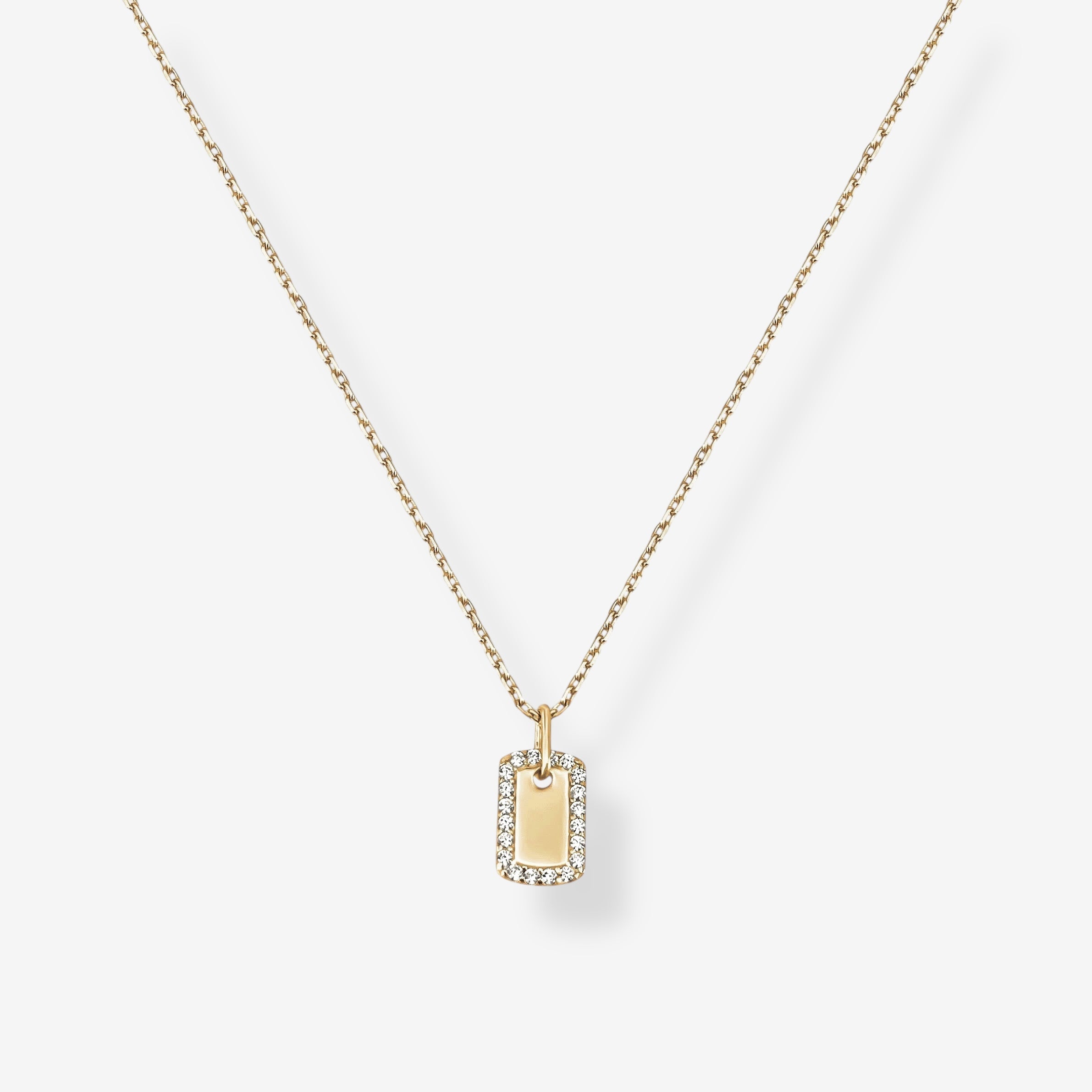 The Dainty Dog Tag Necklace is a delicate gold chain necklace with a small rectangular gold pendant framed by sparkling clear stones, shown on a plain white background.