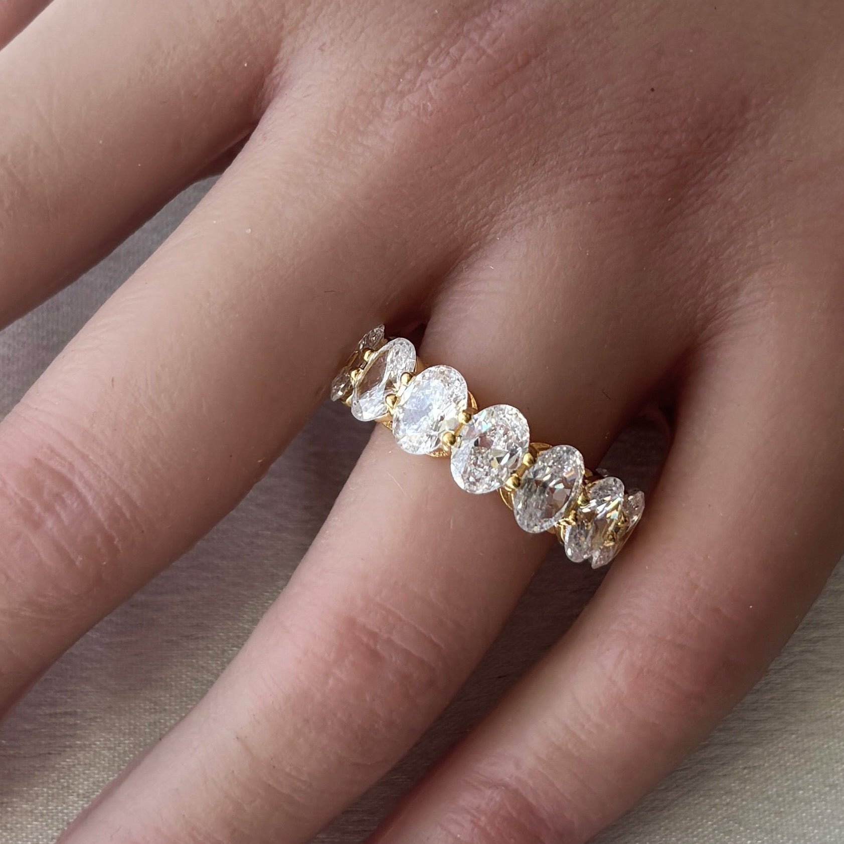 A hand wears the Bella Ring—a 14k gold plated band with large, oval clear gemstones—displayed on the ring finger against a light background.