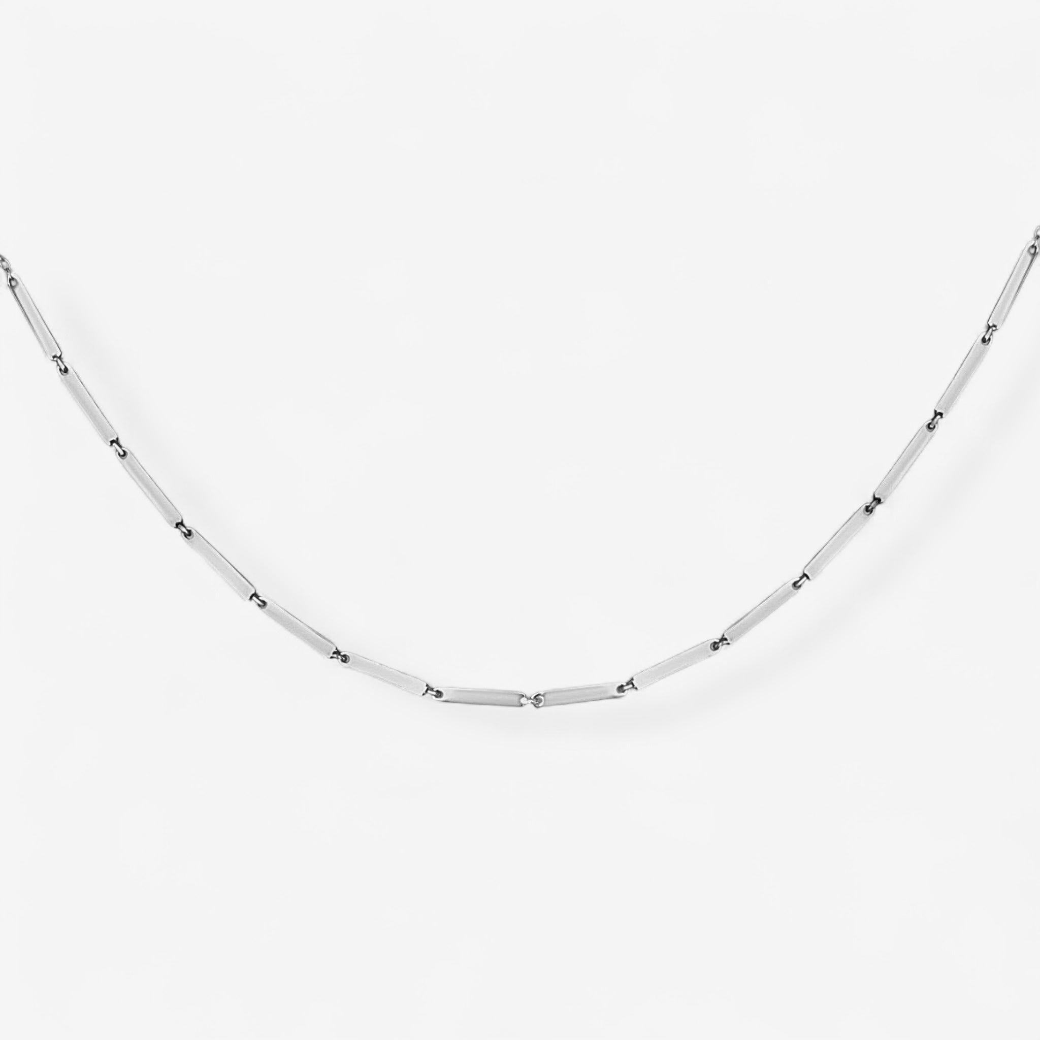 The Emmie Necklace is a delicate minimalist piece featuring a silver chain with evenly spaced thin rectangular links, displayed on a plain white background.