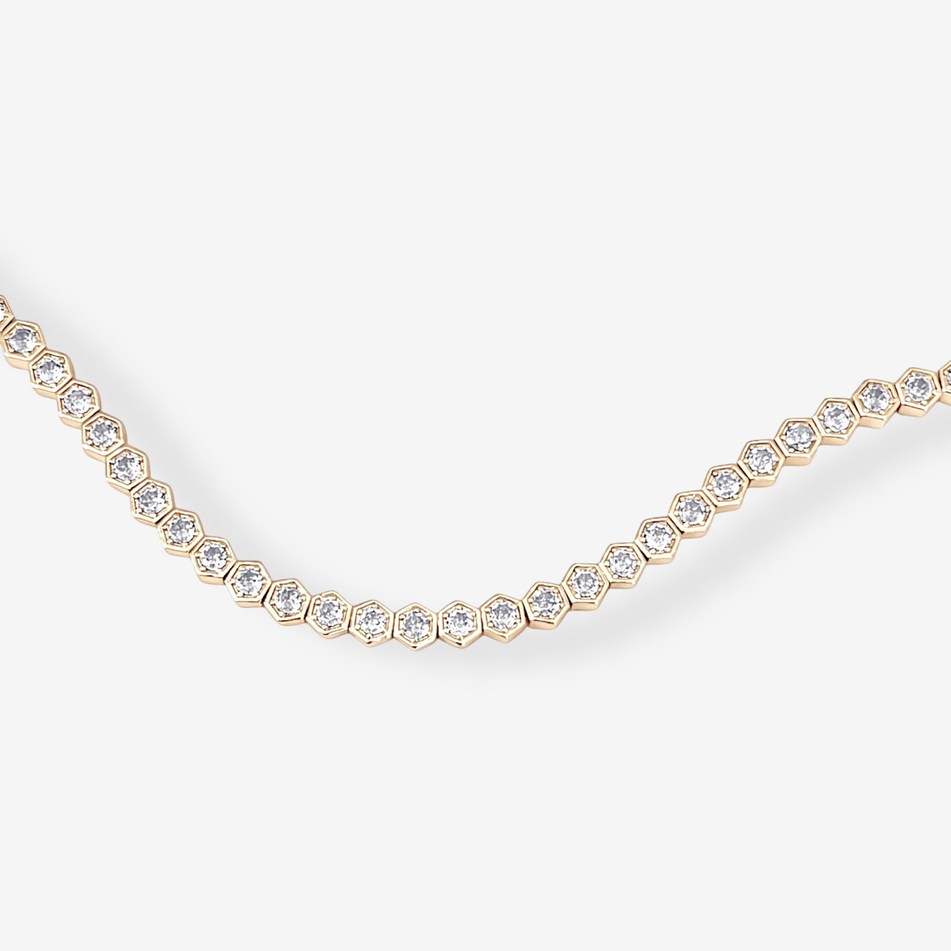The Hexagon Tennis Bracelet features a repeating gold hexagonal pattern, each segment set with a sparkling diamond, elegantly displayed against a white background.