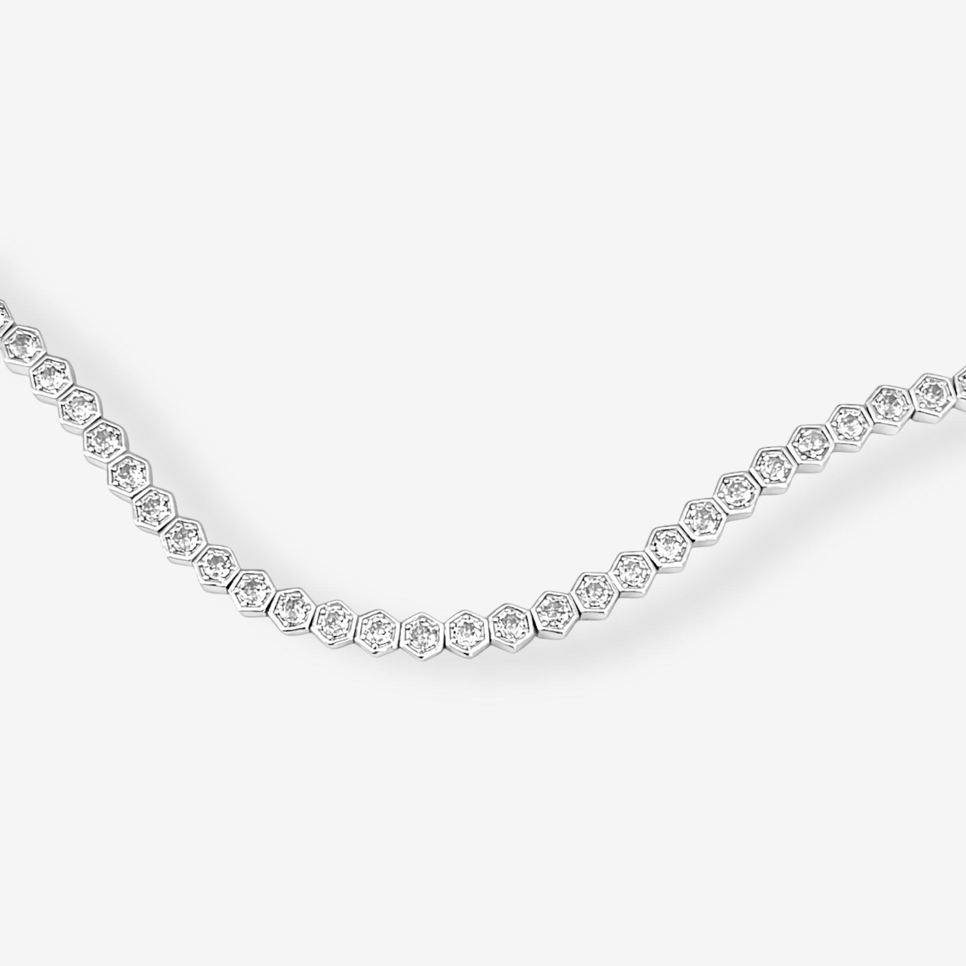 The Hexagon Tennis Bracelet is a silver bracelet with small, hexagon-shaped links, each adorned with a white gemstone, arranged in a delicate, curved pattern on a plain white background.