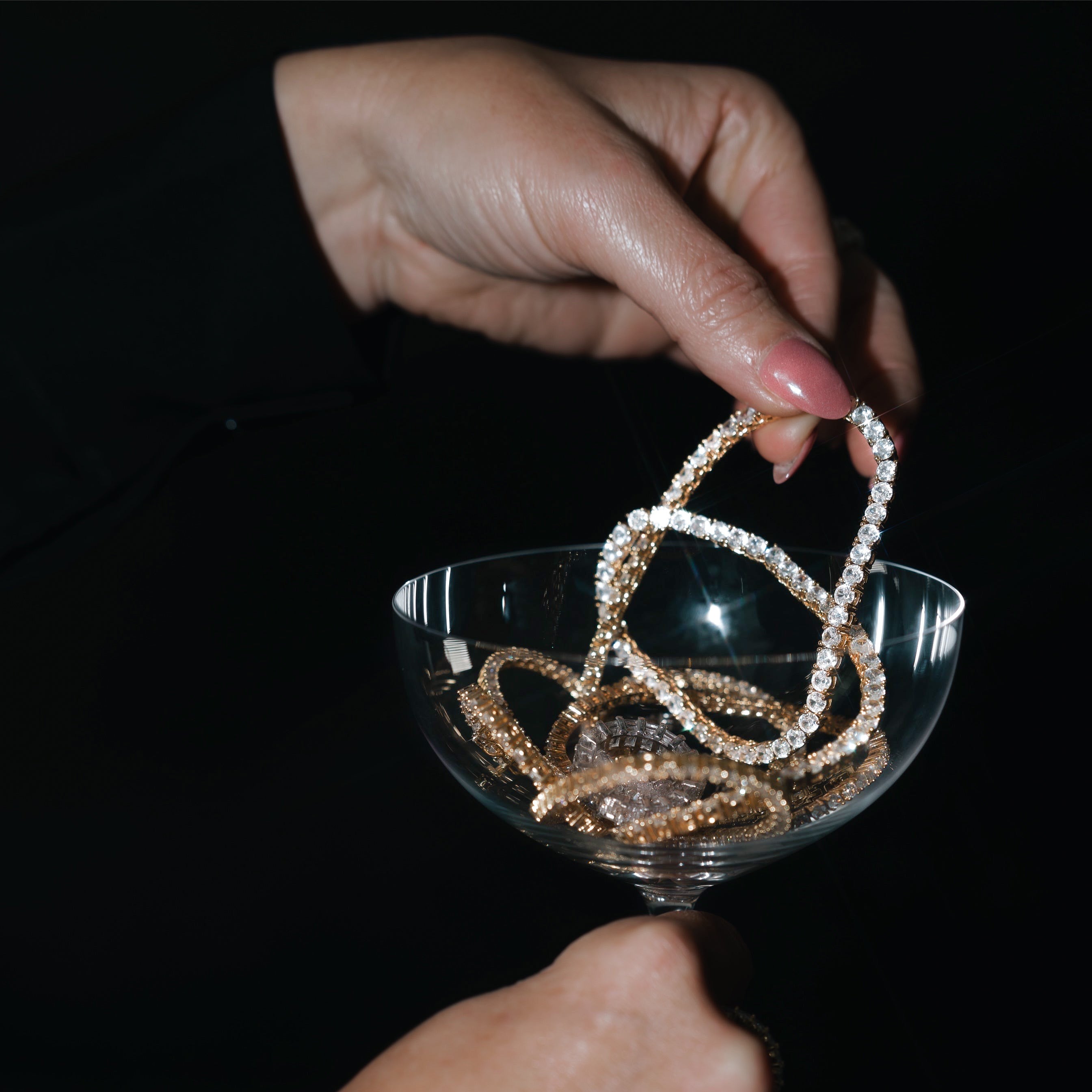 Close up of model holding a martini glass wearing Mia Tennis Necklace in gold showcasing layered simulated diamond chains with polished gold shine and elevated evening style