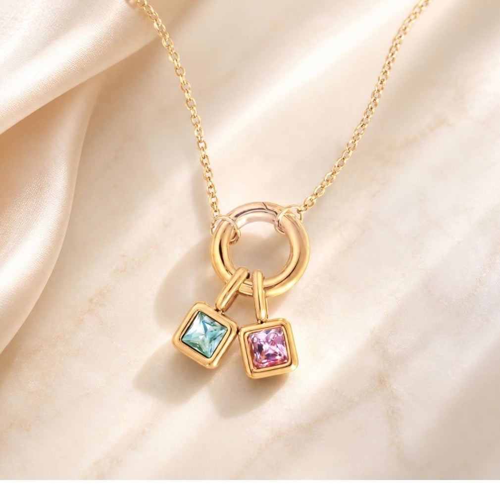 Personalized two birthstone charm necklace in 18k gold with dainty colorful gemstone charms on neutral fabric background