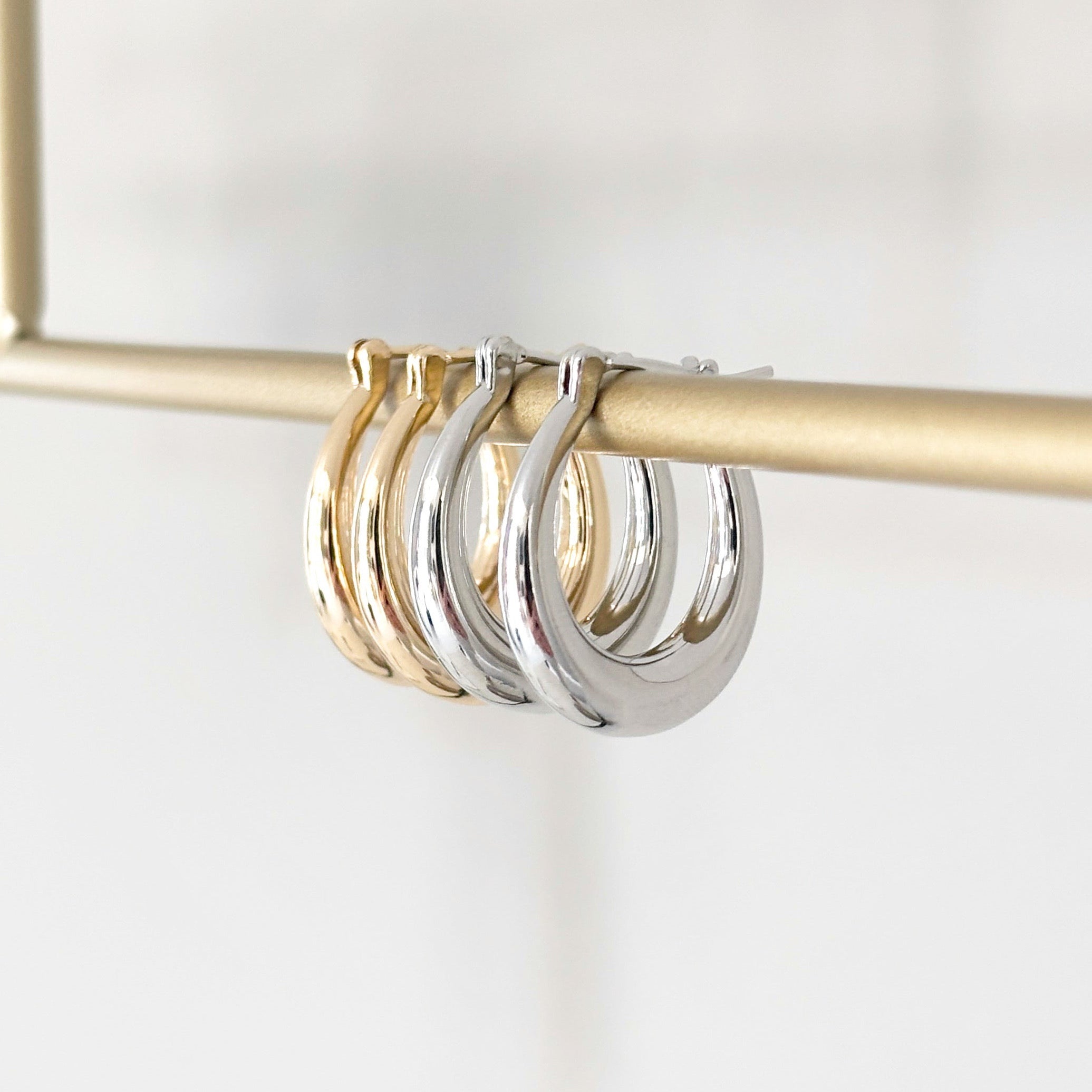 Riley Oval Hoops in silver and gold displayed side by side showcasing sleek oval design and high-shine plated finish